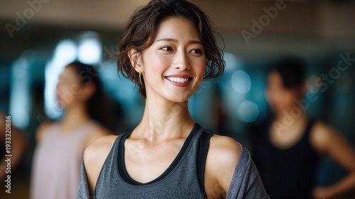 Young Asian woman, short dark hair, smiles warmly in gray athletic tank top, fitness studio, blurred classmates behind. Soft lighting,. Positive, energetic mood. Free Download Young Asian woman, short dark hair, smiles warmly in gray athletic tank top, fitness studio, blurred classmates behind. Soft lighting,. Positive, energetic mood. - GFXLoad