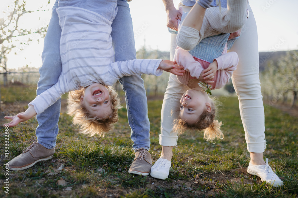 © Halfpoint - Parents lifting children upside down during playful springtime moment.