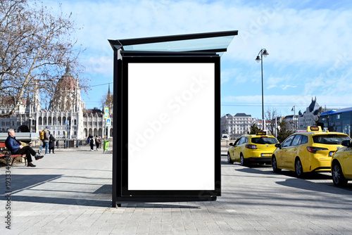 bus shelter at a busstop. blank vertical billboard ad display panel. empty white lightbox sign. city transit station. urban street setting. white outdoor advertising mockup.