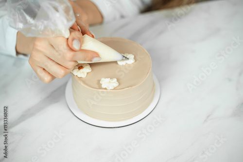 Confectioner decorates cake with cream flowers at a kitchen counter during the day