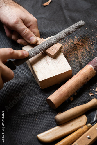 A craftsman makes a string holder from a wooden blank using a round file
