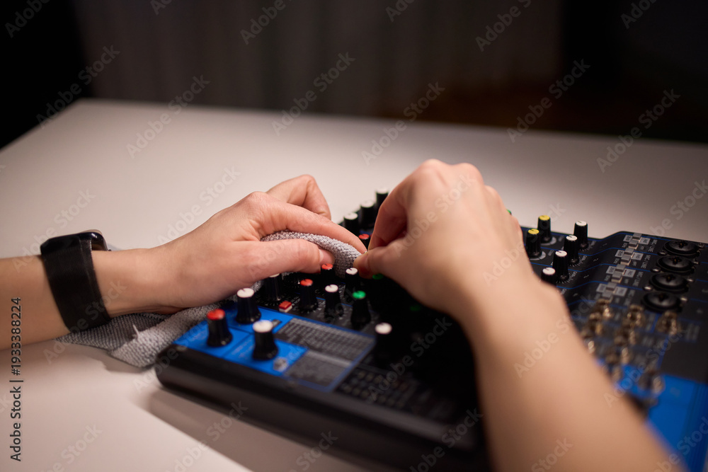 Fototapeta premium Professional cleaning of audio console with soft cloth under warm light. Studio engineer performing routine upkeep on soundboard using gentle motions and accurate wiping