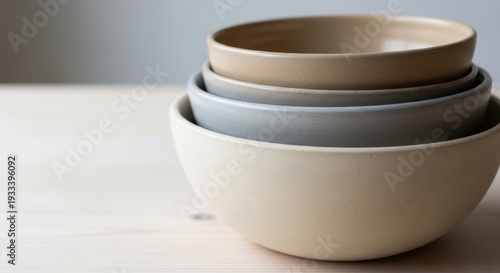 Stack of neutral colored ceramic bowls resting on a wooden table with copy space. Minimalist dinnerware and kitchen utensil for quiet luxury home.
