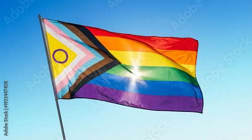Waving flag with rainbow stripes and diverse colors against a blue sky, representing the LGBTQ+ community, inclusion, and identity expression