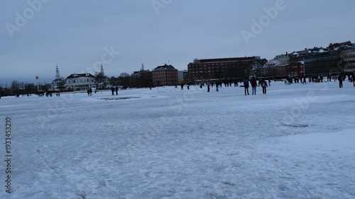 A winter landscape of Copenhagen, Denmark. The photograph depicts a wide, snow-covered square, or frozen urban space, in the center of the capital, where people stroll on a cold winter day