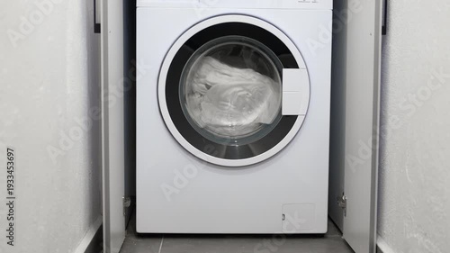 Modern washing machine spinning clean laundry. White clothes and laundry spinning inside the drum of a modern washing machine during a wash cycle. Household appliance working to clean textiles