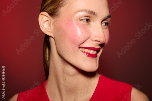 Картината върху платно Smiling woman with shiny skin and red lipstick looks sideways on red background