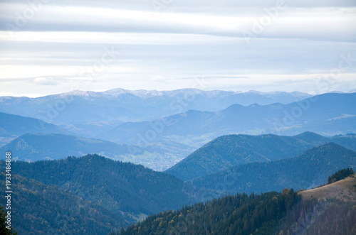 Soft blue layers of mountains and forested hills recede into a misty valley beneath an overcast sky, conveying calm, remoteness and serene natural beauty. Carpathians, Ukraine