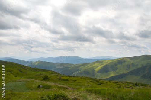 Peaceful panoramic mountain landscape showing green ridges, forested valleys and dramatic white clouds under a blue sky, evoking tranquility, adventure and natural beauty for travel and outdoor themes