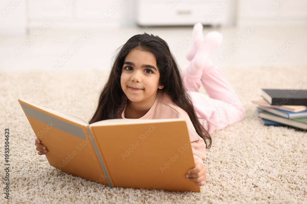 Naklejka premium Cute little girl reading book on floor at home