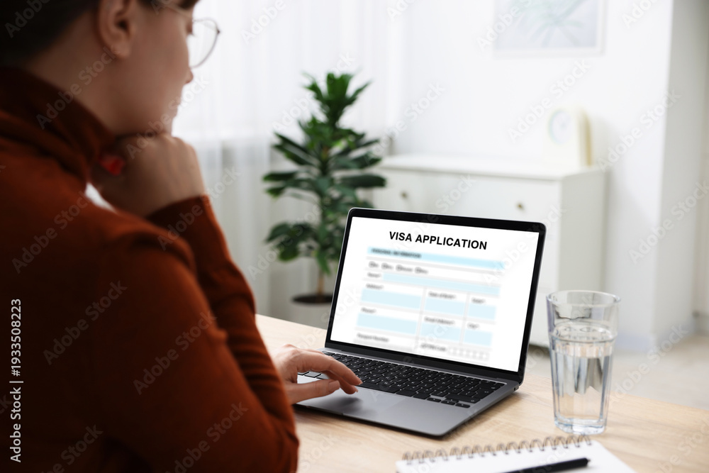 Obraz premium Visa application. Woman using laptop to fill in online form at table, closeup