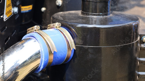 Rubber hose with clamp. Close-up of the blue soft rubber hose connecting the black air filter and engine with two clamps with selective focus.