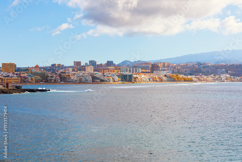 Expansive Las Canteras Beach in Las Palmas de Gran Canaria, Spain, showing city skyline along water's edge. Calm Atlantic Ocean Leading to a long stretch of urban coastline and distant mountains