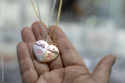 Two necklaces with heart-shaped pendants for mother and daughter displayed in a hand during a shopping trip in a jewelry store