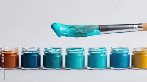 Paintbrush dipped in cyan ink, hovering over a full CMYK ink set, white background