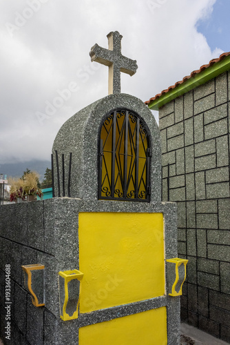 Grave marker with cross and yellow accents in a cemetery under a cloudy sky