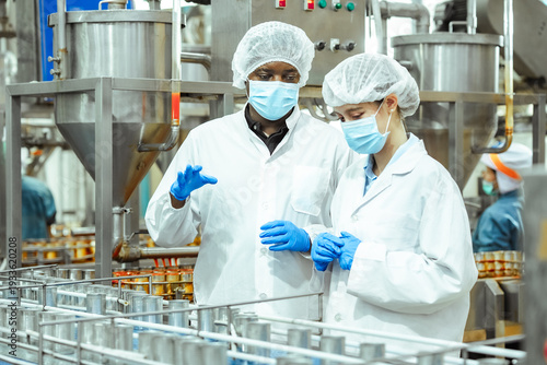 Canvas Print Food safety supervisors discuss canned seafood production line while monitoring conveyor system inside regulated processing plant, ensuring HACCP compliance and contamination prevention standards