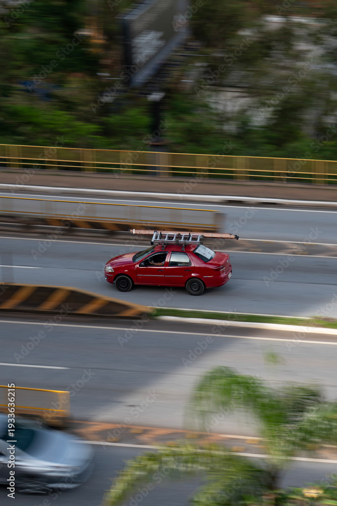 Fototapeta premium Red Fiat Siena side profile in motion, Compact work sedan driving on city avenue