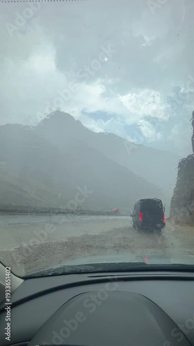 Vertical format of extreme weather captured from point of view of a driver pulled over on the side of the highway due to sudden intense, rapid rainfall. With mountains and heavy clouds in view.