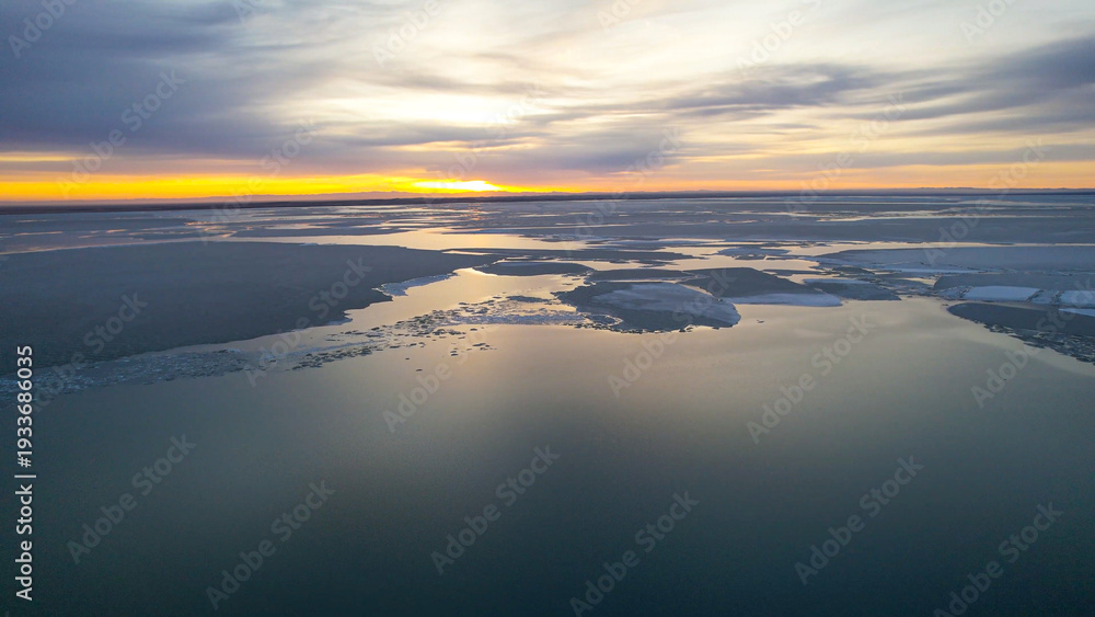 Fototapeta premium Aerial Frozen Lake Dotted With Islands, Ecologist Mapping Island Habitats And Shoreline Ice, Scattered Dark Islets Contrast With Smooth Ice Sheets, Low Winter Light And Clear Coastal Geometry.