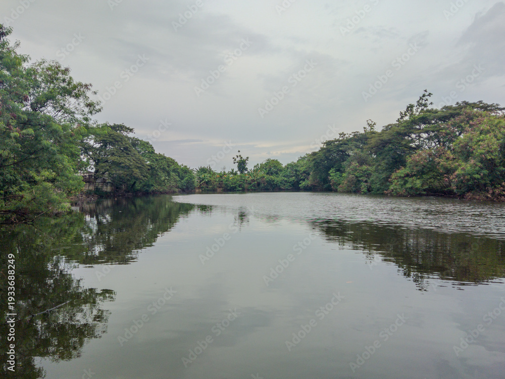Fototapeta premium Serene Artificial Lake with Gentle Water Ripples Surrounded by Lush Green Trees