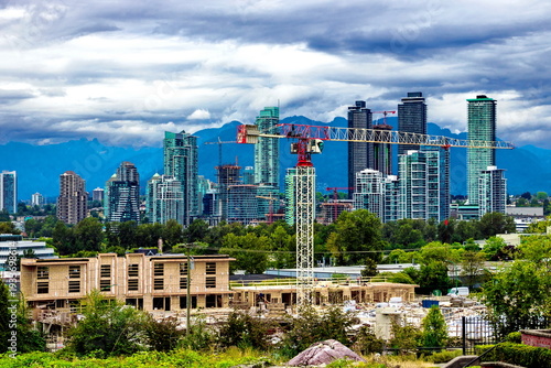 
Construction of new timber townhouses in a residential area of ​​Burnaby. Behind the construction site is a residential area of ​​high-rise buildings with a mountain range in the background 
