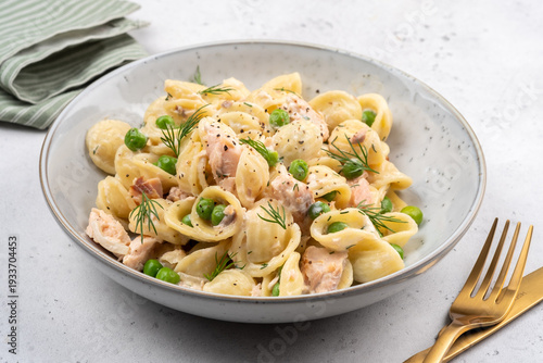 Pasta with chicken and peas on a white plate served for lunch on a table with golden fork