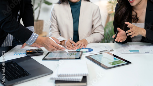 Photos Professional business team collaborating and analyzing financial reports on digital tablets and documents at a modern office desk