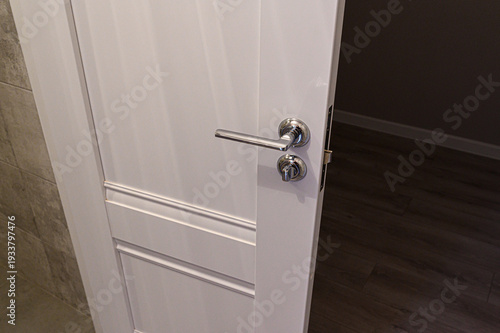Fotografia A white interior door with a sleek chrome lever handle and lockset; features cla