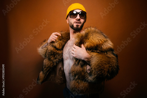 Man posing with furry jacket yellow beanie sunglasses