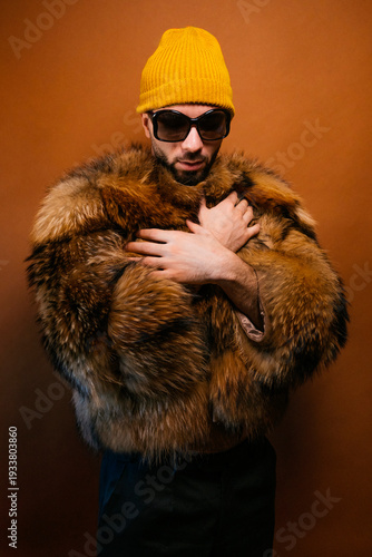 Stylish man wearing a yellow beanie, sunglasses, and fur coat