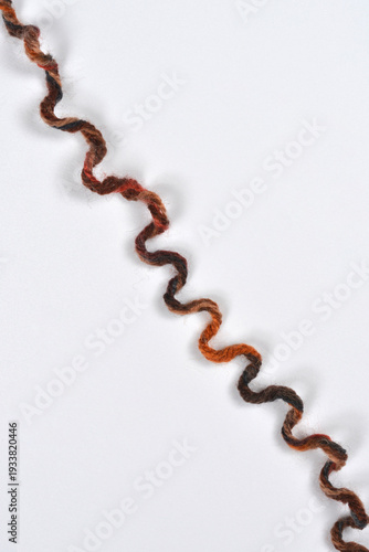 A vertical overhead shot shows a single strand of thick, curly, multicolored brown and orange wool yarn running diagonally across a plain gray background