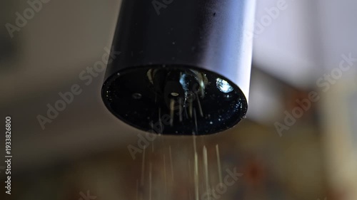 Closeup view of electric pepper grinder milling black pepper. Kitchen appliance crushing spice with rotating mechanism during cooking.