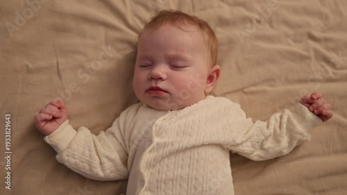 A newborn baby lying on its back and sleeping on a neutral blanket