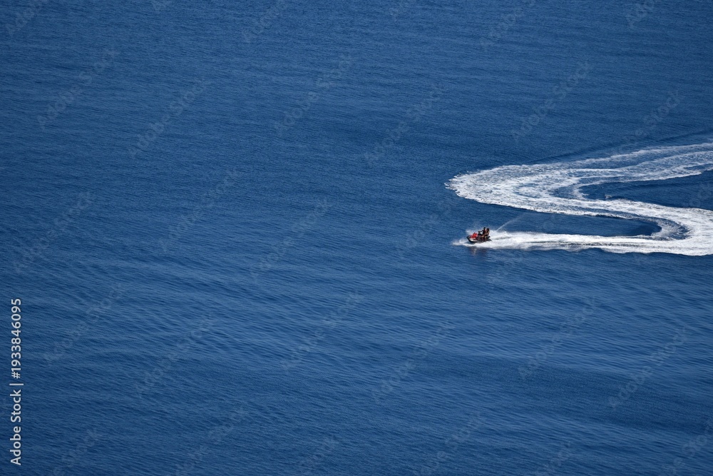 Naklejka premium Seascape with scenic view of a young couple on a jet ski cruising on the waters of Therasia island in Cyclades, South Aegean Greece.