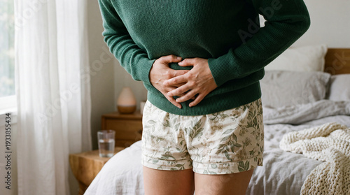 Woman in pajamas experiencing severe stomach pain or abdominal cramps at home, indicative of digestive issues or menstrual discomfort