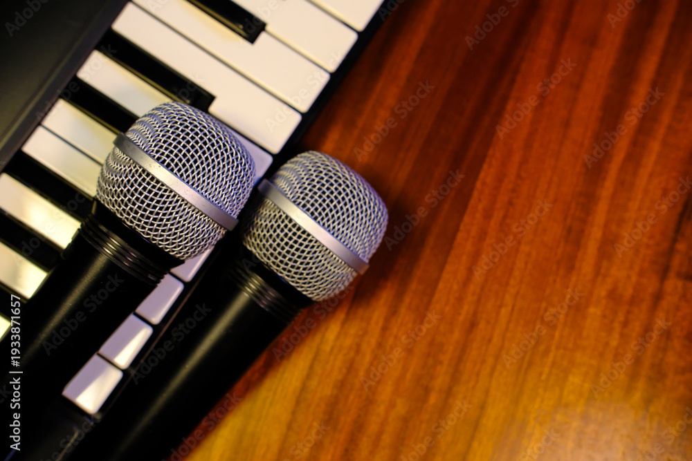 Obraz premium Microphones on piano keyboard with wooden background, music and singing concept.