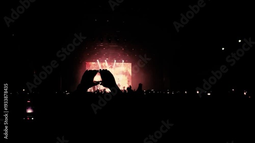Crowd filming live concert with smartphone – golden stage lights and cheering audience.