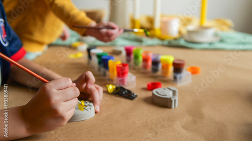 Children's hands painting small objects with colorful paints on a craft table