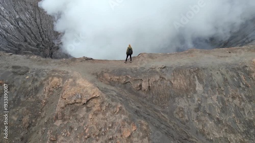 Aerial view of woman walking along the rim of steaming Mount Bromo volcano crater in Indonesia. Concept of nature, travel, adventure, and breathtaking landscapes.