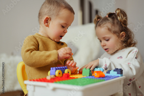 Fotografie Two young children sit at a table, building with colorful blocks