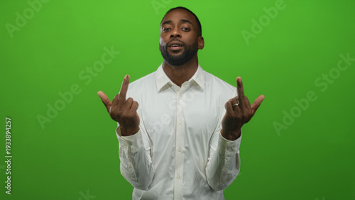 Fényképezés Man showing middle fingers to camera in green studio wearing a white shirt with visible beard and direct gaze; defiance