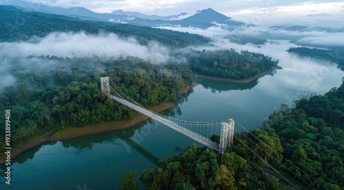 Aerial view of a bridge spanning a lake amidst dense, green forests shrouded in mist and clouds