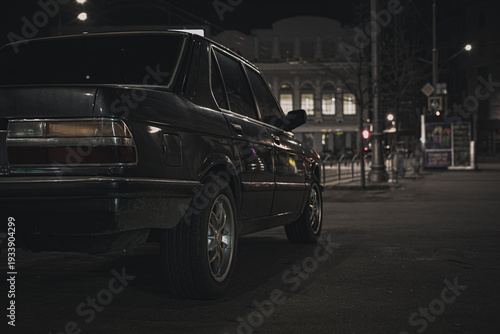 Rear view of a classic blue sedan parked on a night city street: vintage automobile under urban street lights and night atmosphere.