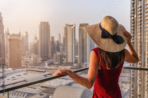 A elegant woman in a red dress enjoys the sunset view over the skyline of Downtown Dubai, UAE, from her balcony