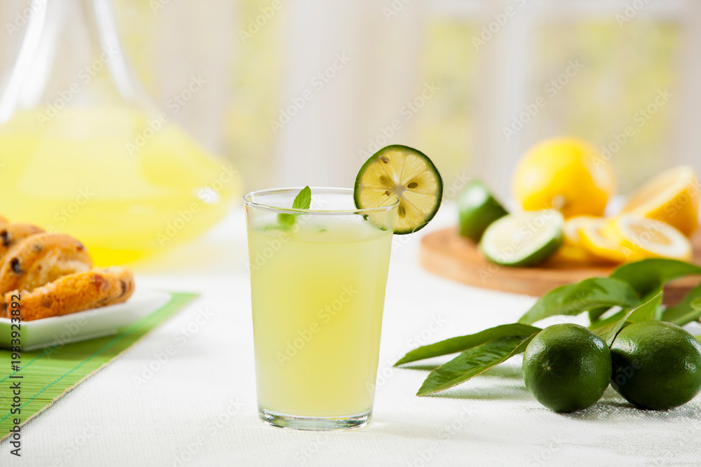 Fototapeta premium Fresh homemade lemonade or lime juice in a glass with lemon and lime slices on a wooden board, bright garden background.