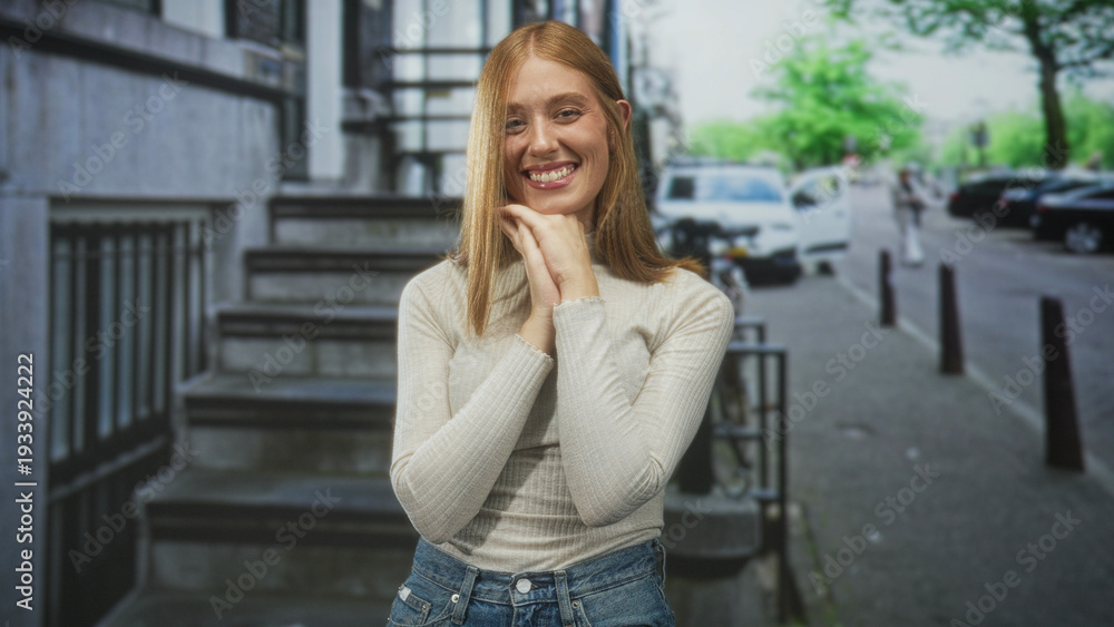 Fototapeta premium Woman clasping hands near chin smiling on stone steps by sidewalk with parked cars on city street; gentle joy.