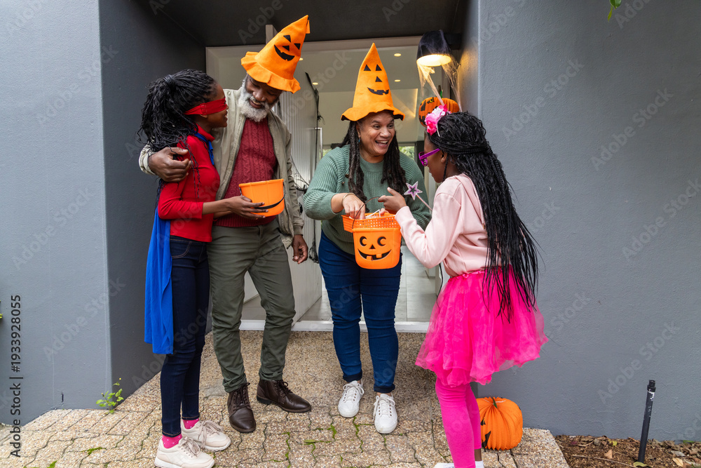 Obraz premium African American family standing at home doorway holding jack-o'-lantern buckets in pumpkin hats