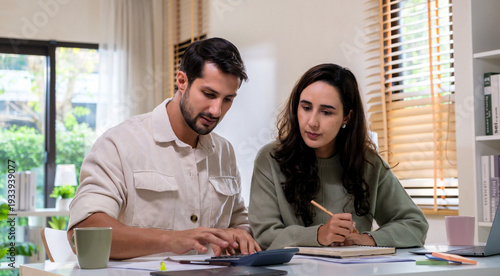 Couple reviewing personal financial calculate tax document while checking expense and payment at home, inspecting bills, budget, insurance, and monthly planning discussion with laptop