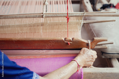 Thai woman weaving colorful silk fabric with ancient technique in rural village.